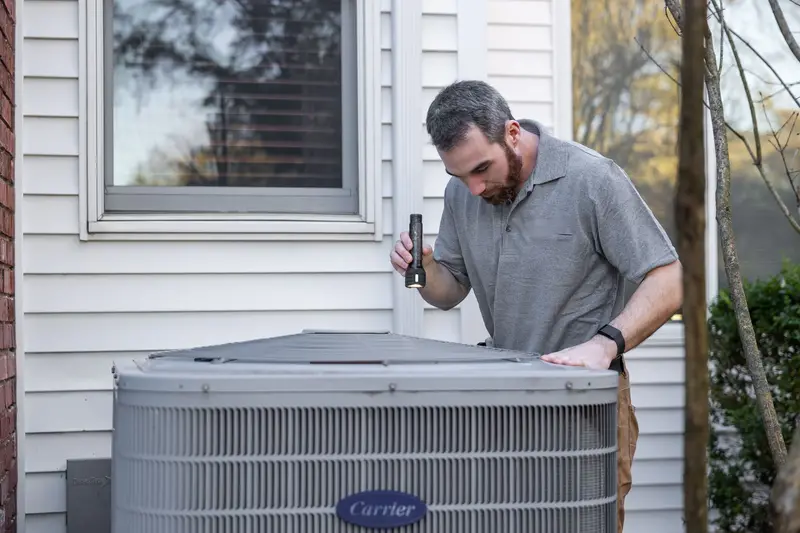 Technician with a flashlight looking over a home's outdoor AC unit