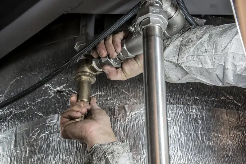 Plumber's hands tightening a valve fitting on pipes under a sink